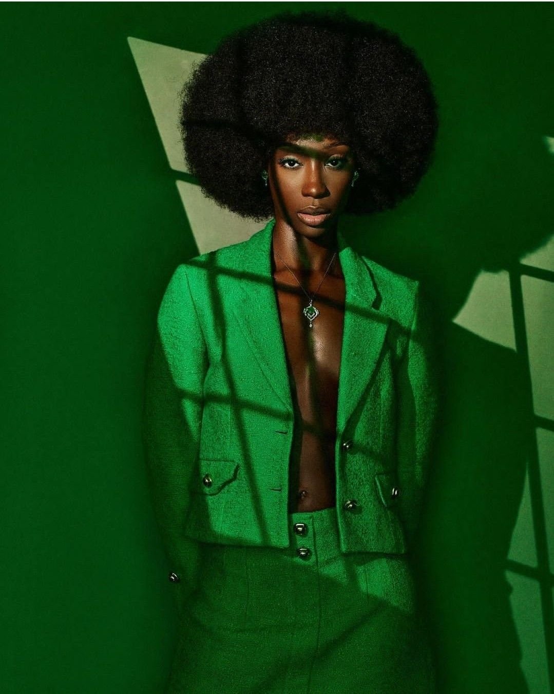 Portrait in an emerald blazer and afro, dramatic window-shadow lighting against green